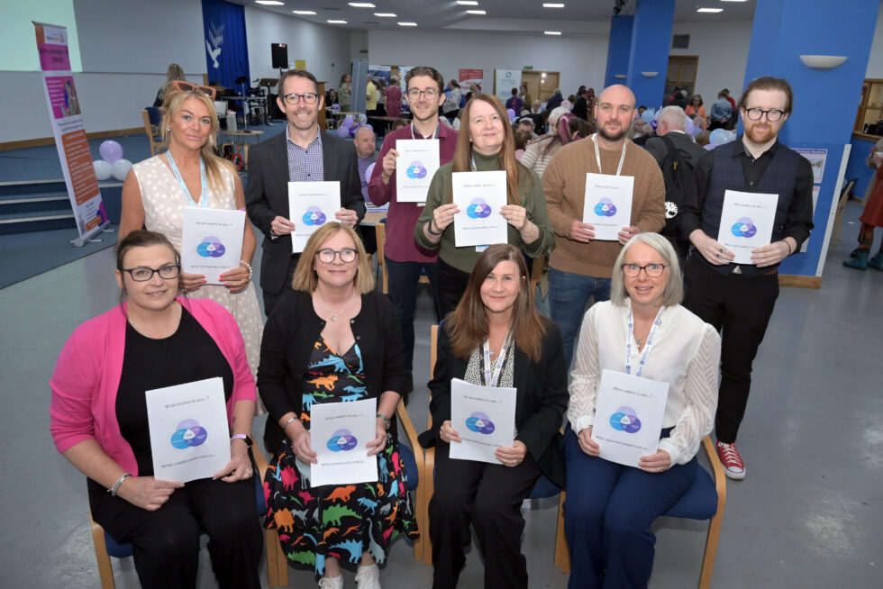 Representatives from the community and Health & Social Care North Lanarkshire stand at the back and sit at the front holding documents to gather people's views.